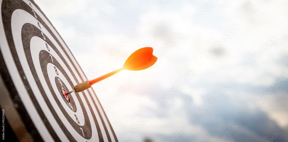 Close up shot red darts arrows in the target  of dartboard center on dark blue sky background. Busin