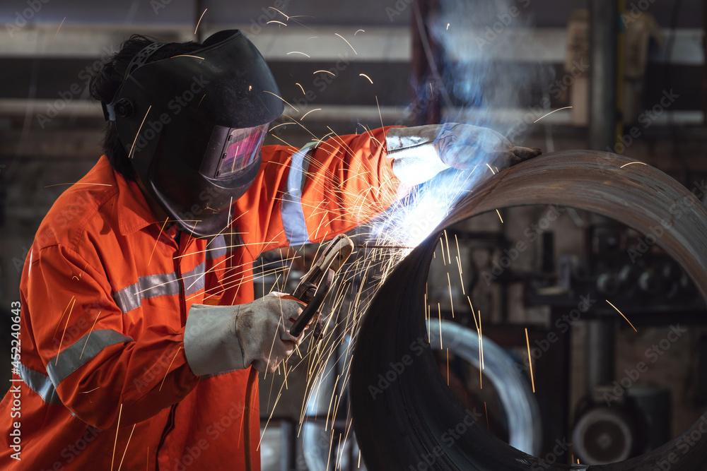 A Worker with protective mask welding metal pipe in a factory