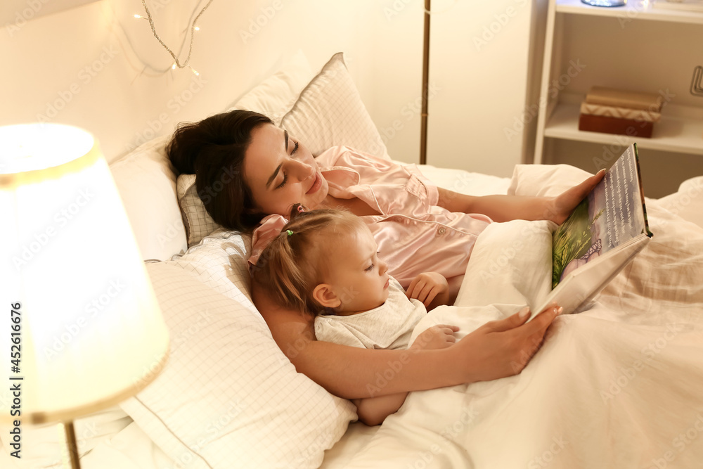 Mother and little baby reading book in bed