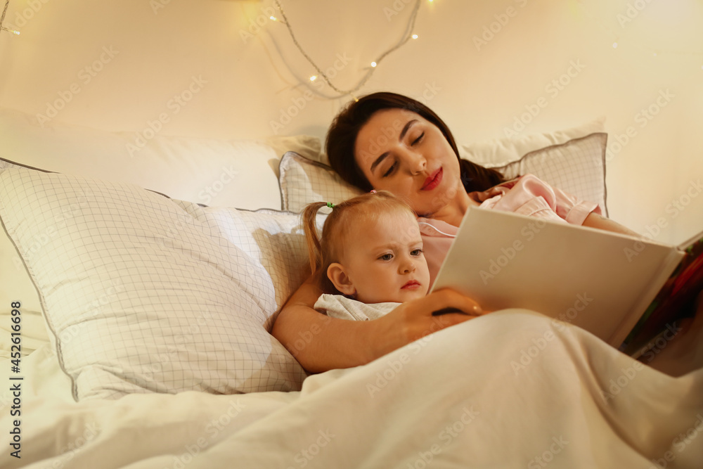 Mother and little baby reading book in bed