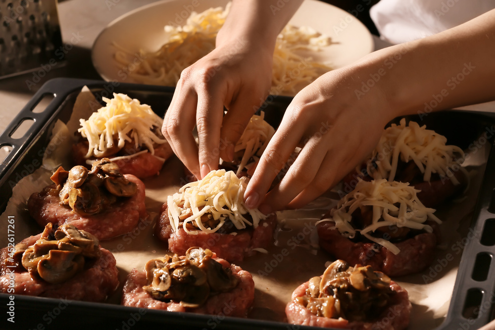 Woman adding grated cheese on minced meat boats with mushrooms, closeup