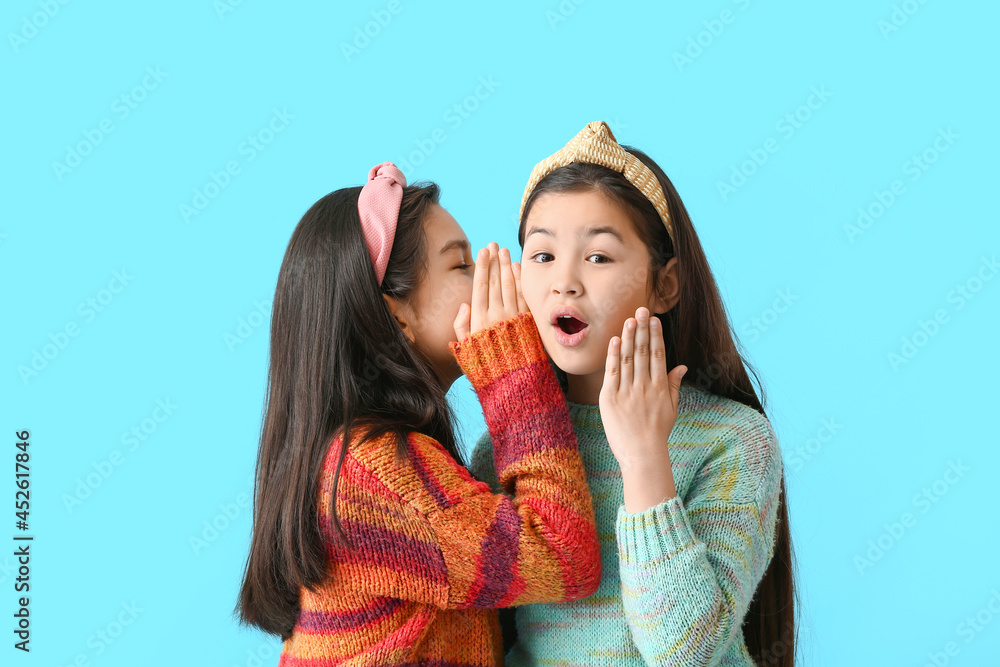 Cute little girls telling secrets to each other on color background