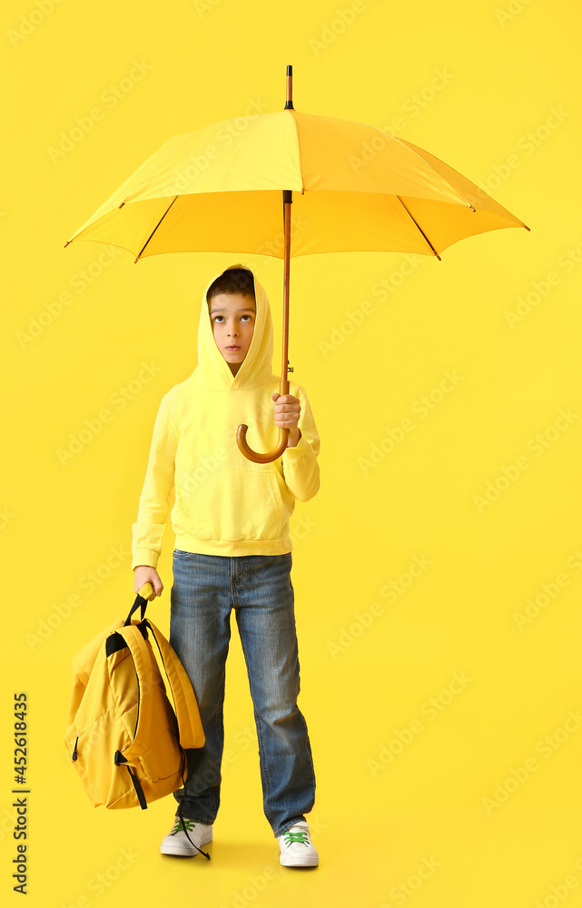 Little schoolboy with backpack and umbrella on color background