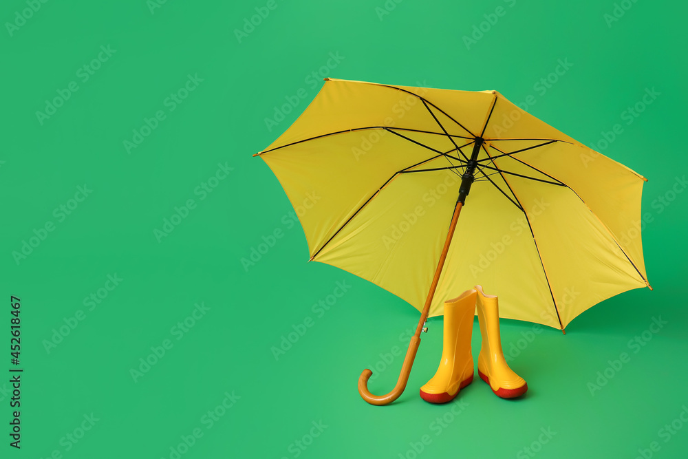 Stylish umbrella with gumboots on color background