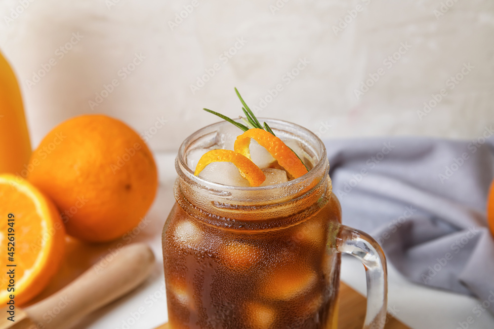 Mason jar of tasty coffee with orange juice on light background, closeup