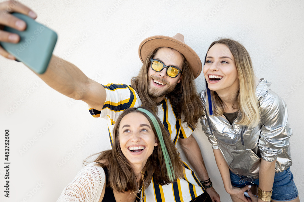 Young stylish friends have fun, taking selfie photo on phone on a white background. Millennials or g