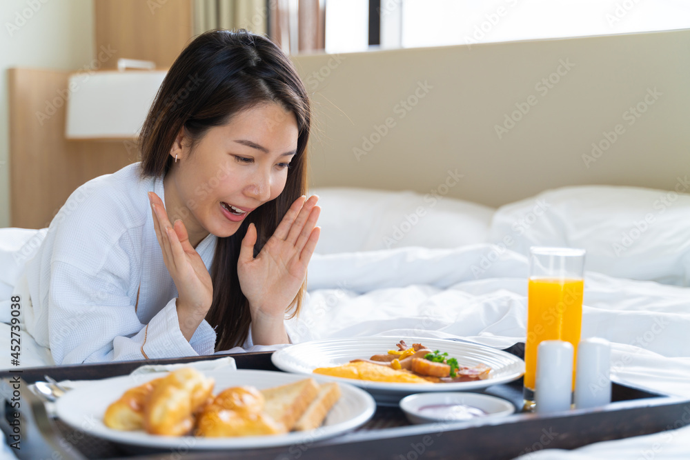 穿着浴袍的亚洲年轻美女在卧室的床上享用早餐