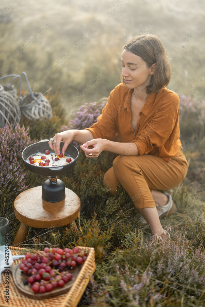 女旅行者在山上旅行时准备早餐，在炉子上煎鸡蛋和葡萄