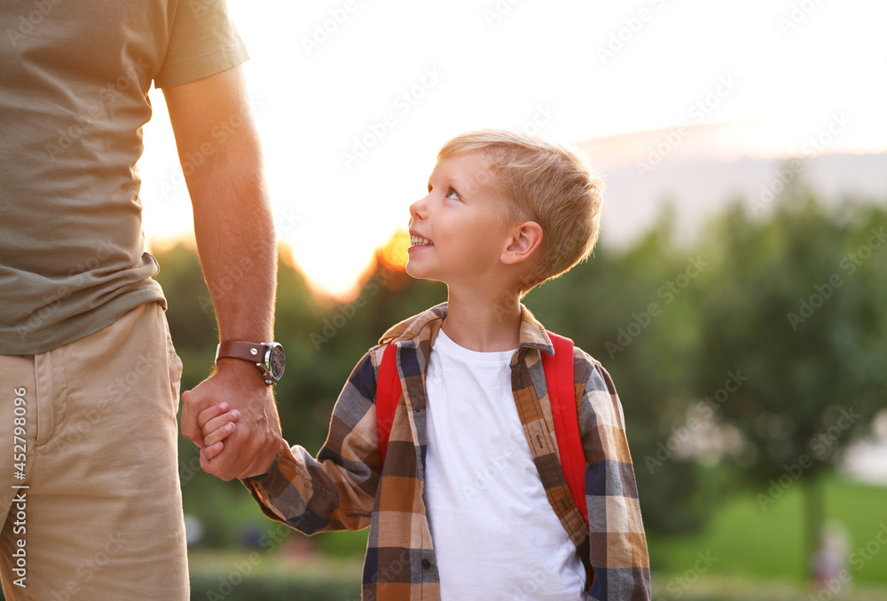 Schoolboy looking at dad with smile while going to first grade in school on sunny autumn day