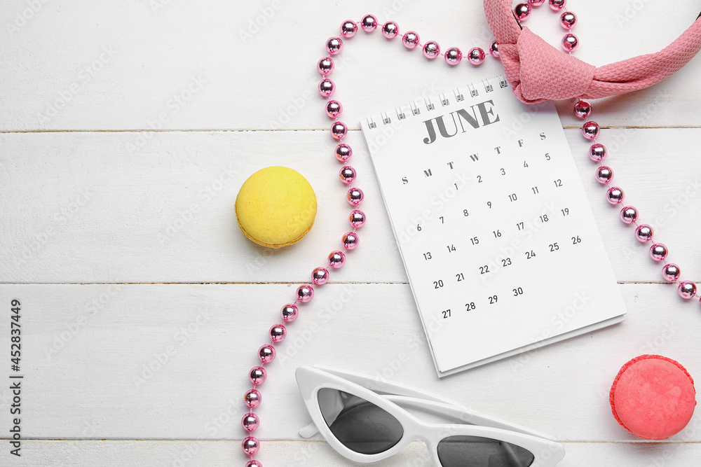 Calendar with macaroons and female accessories on light wooden background