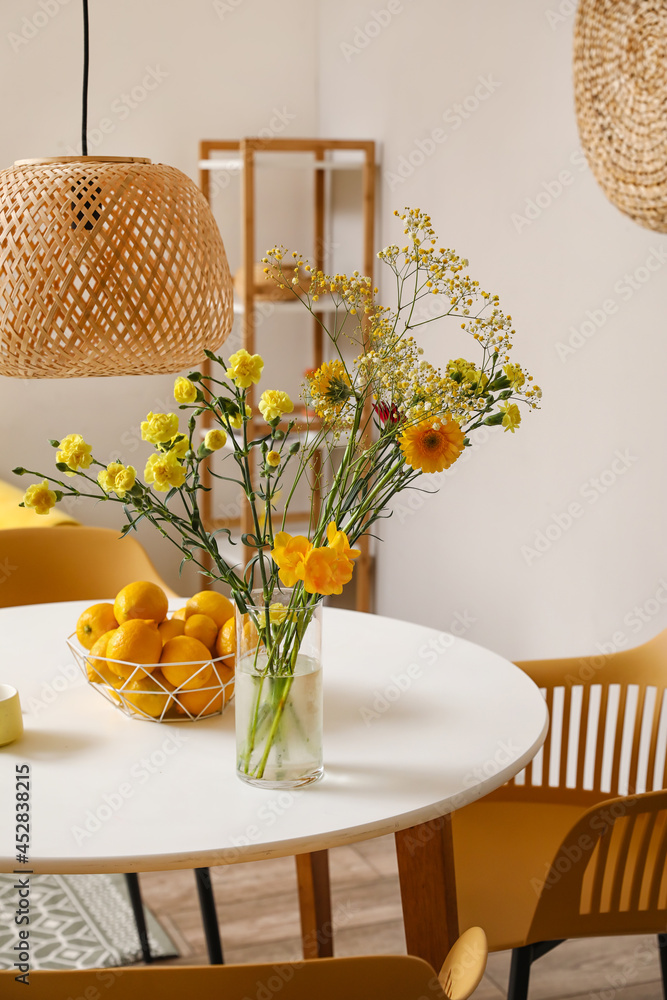 Vase with flowers and lemons on dining table in room