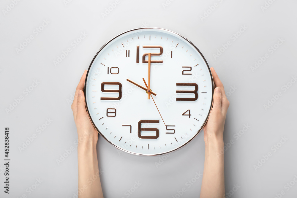 Female hands and stylish clock on light background