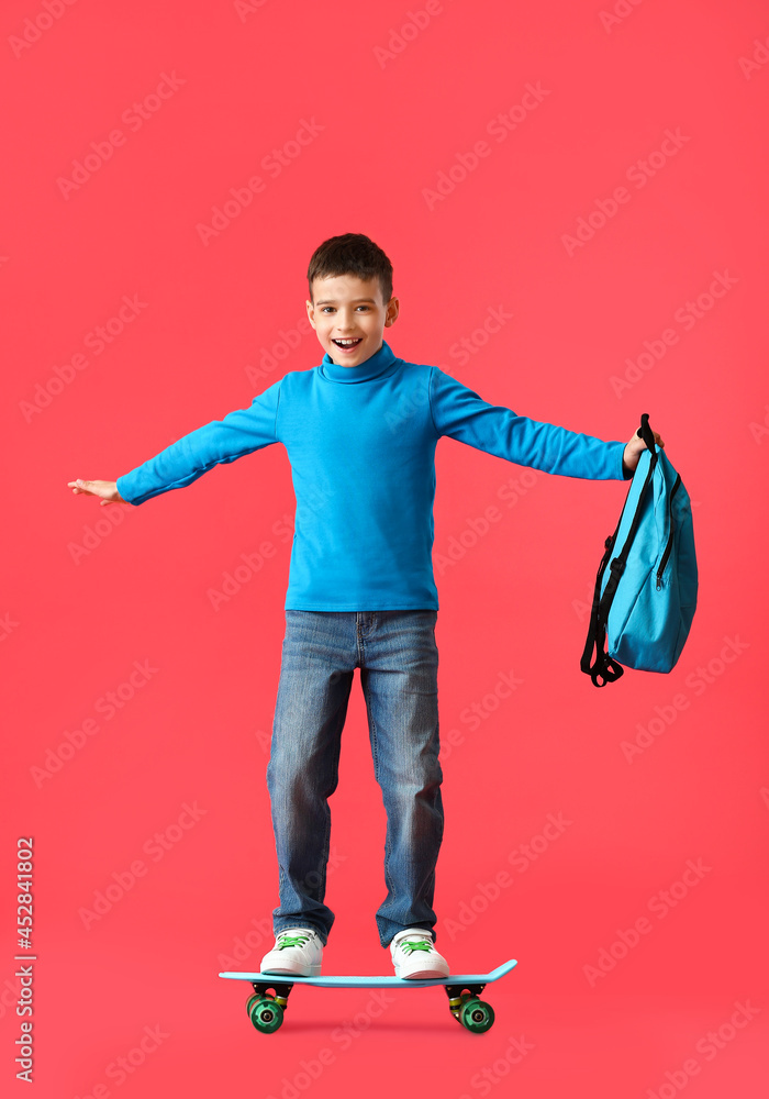 Little schoolboy with backpack and skateboard on color background