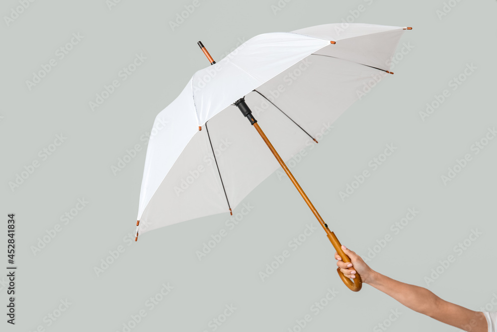 Female hand with open umbrella on light background