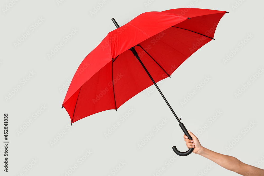 Female hand with open umbrella on light background