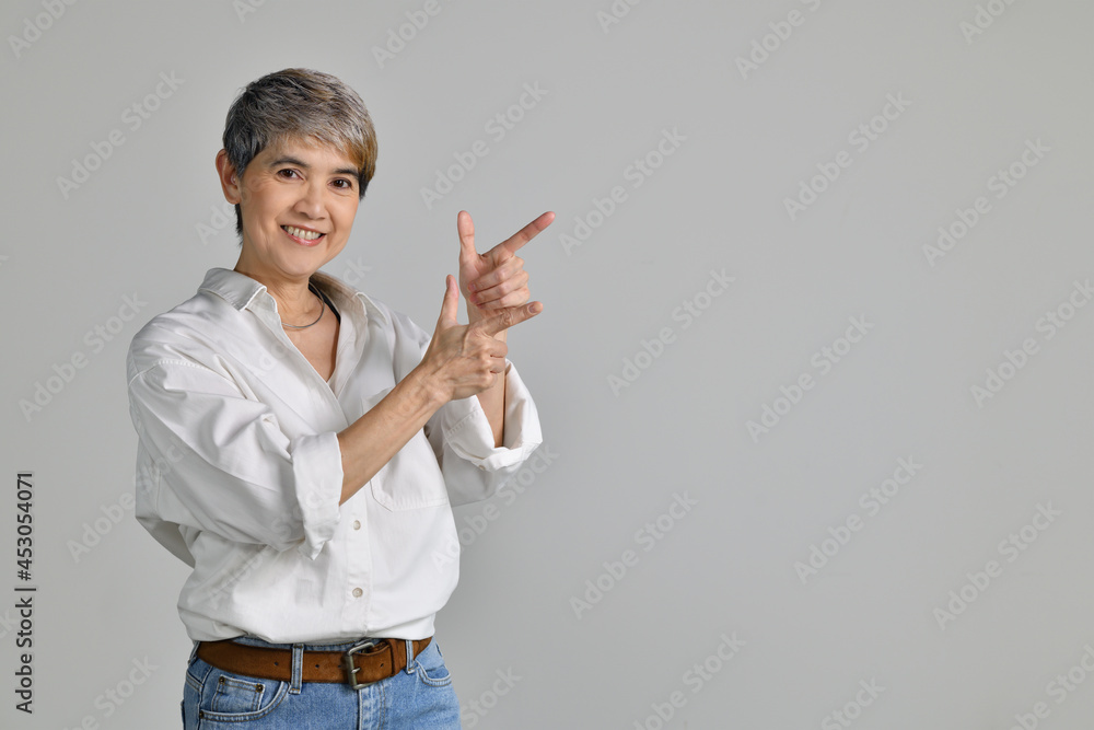 Middle aged Asian woman pointing fingers up at empty copy space for text isolated on white backgroun