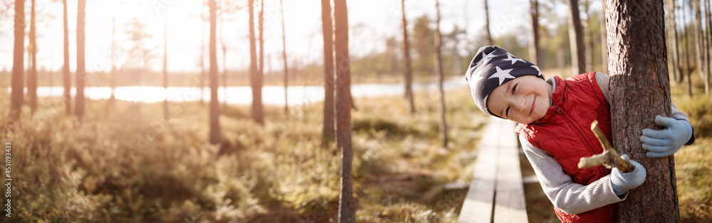 Cute boy in the forest hugging a trees trunk