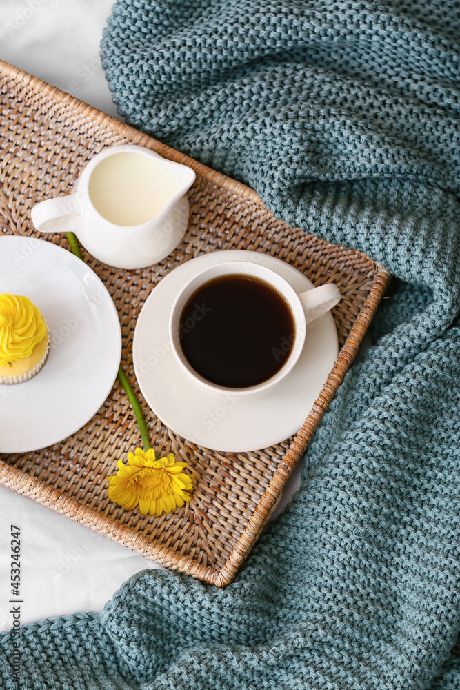 Tray with cup of coffee, cupcake and milk on bed