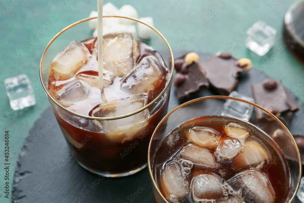 Pouring milk into glasses of tasty iced coffee on table