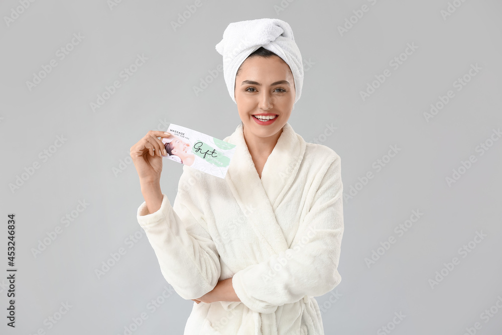 Young woman with gift certificate for massage on light background