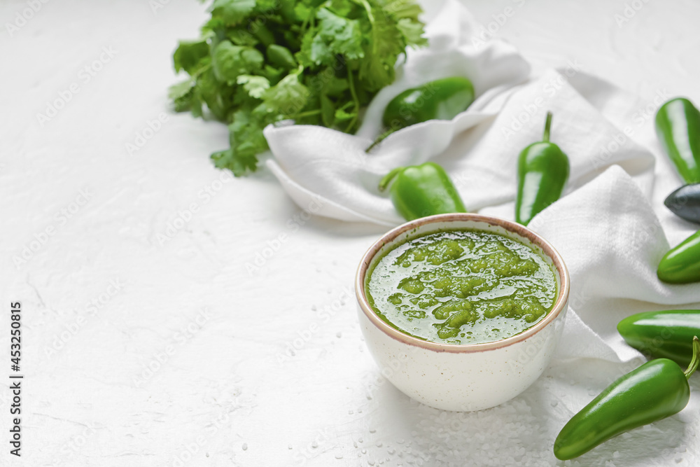 Bowl of Tomatillo Salsa Verde sauce and jalapeno pepper on light background