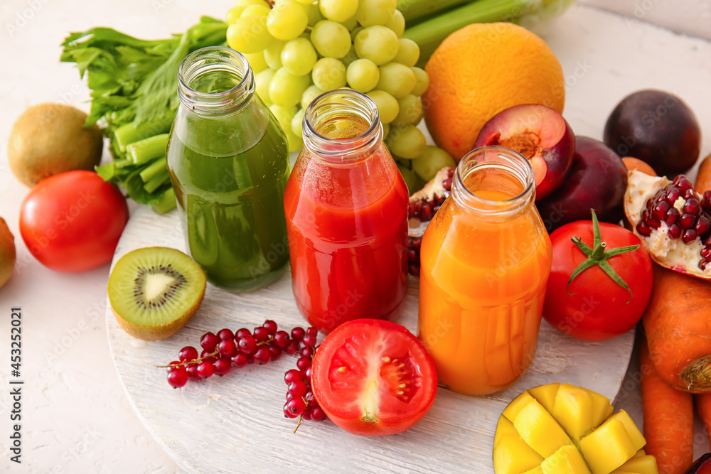 Bottles with healthy juice, fruits and vegetables on light background