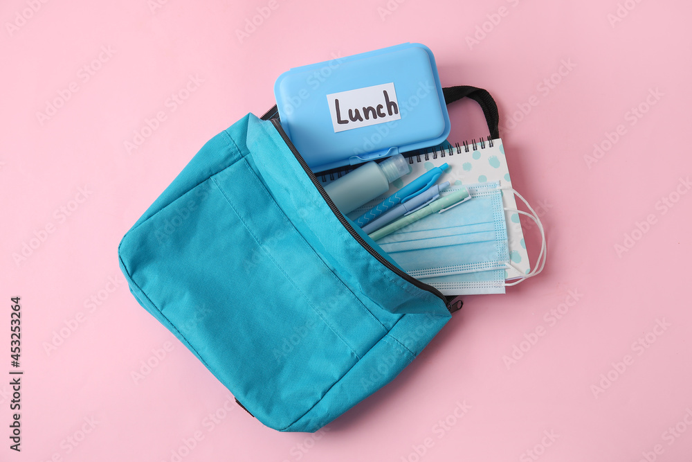 Backpack with lunch box and medical mask on color background