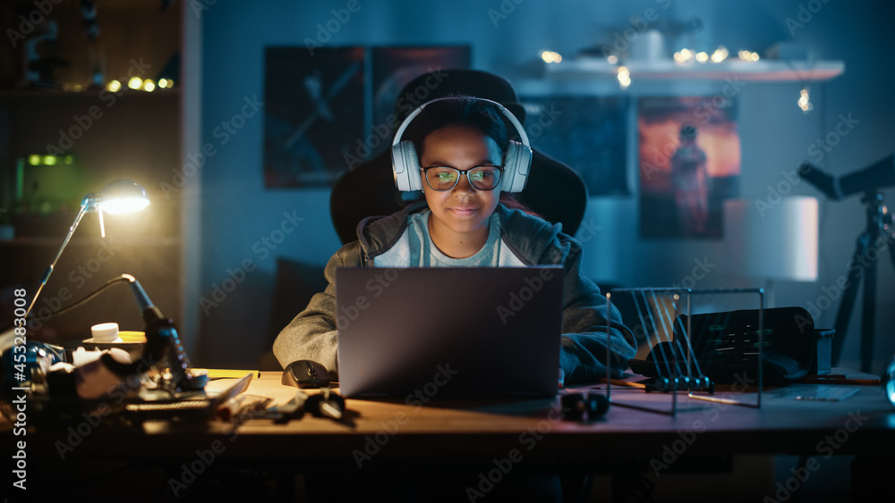 Young Teenage Multiethnic Girl Using Laptop Computer and Wearing Headphones in a Dark Cozy Room at H