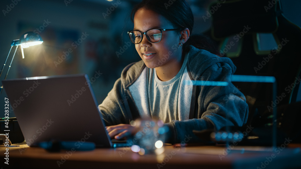 Young Teenage Multiethnic Black Girl Using Laptop Computer in a Dark Cozy Room at Home. Shes Browsi