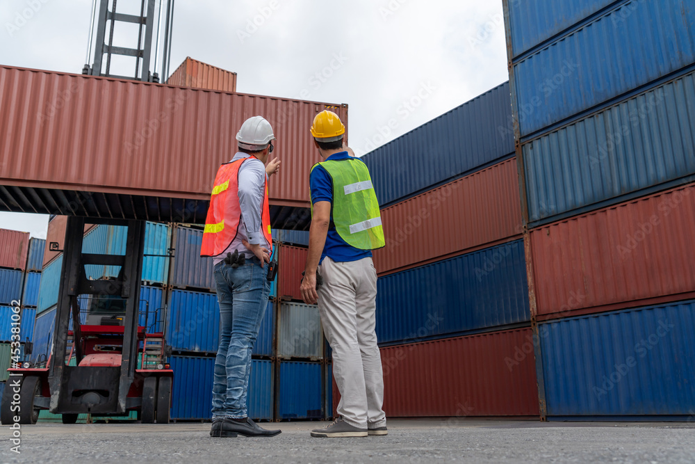 Industrial worker works with co-worker at overseas shipping container yard . Logistics supply chain 