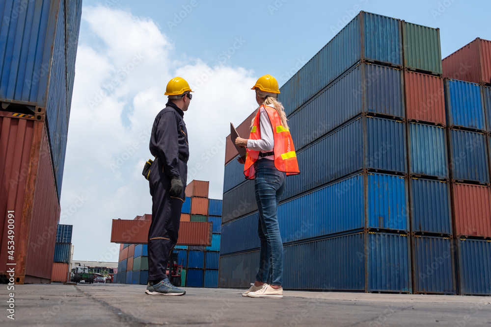 Industrial worker works with co-worker at overseas shipping container yard . Logistics supply chain 