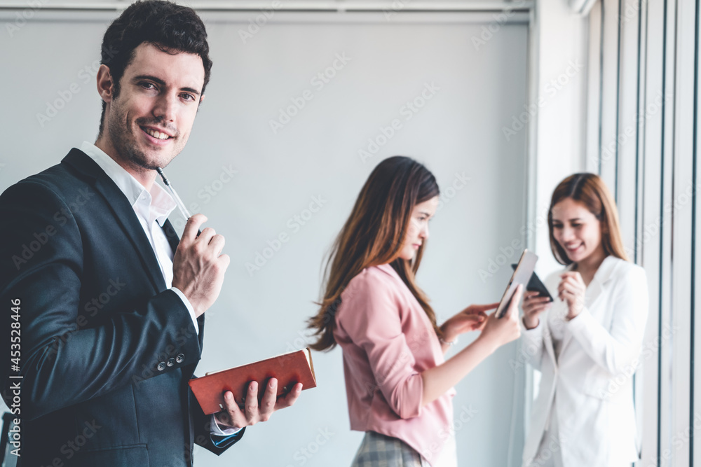 Happy young handsome businessman reading book and working in office with colleagues and friend at wo