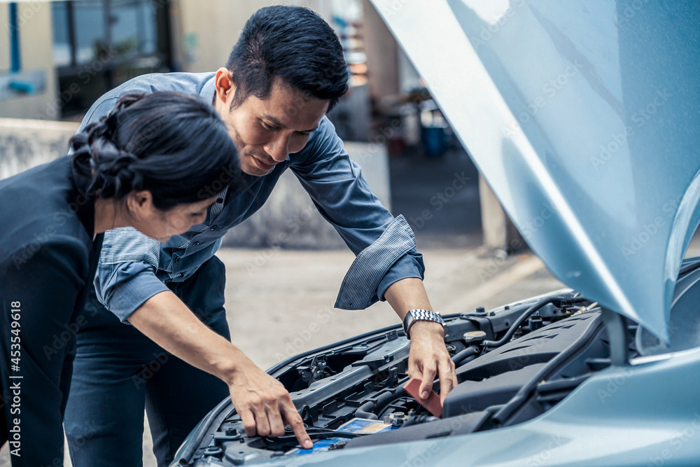 Man help woman fix the car problem. He pop up the car hood to repair the damaged part.