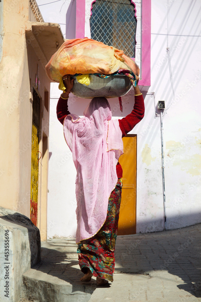 indian woman wearing saree walking with basket on her head