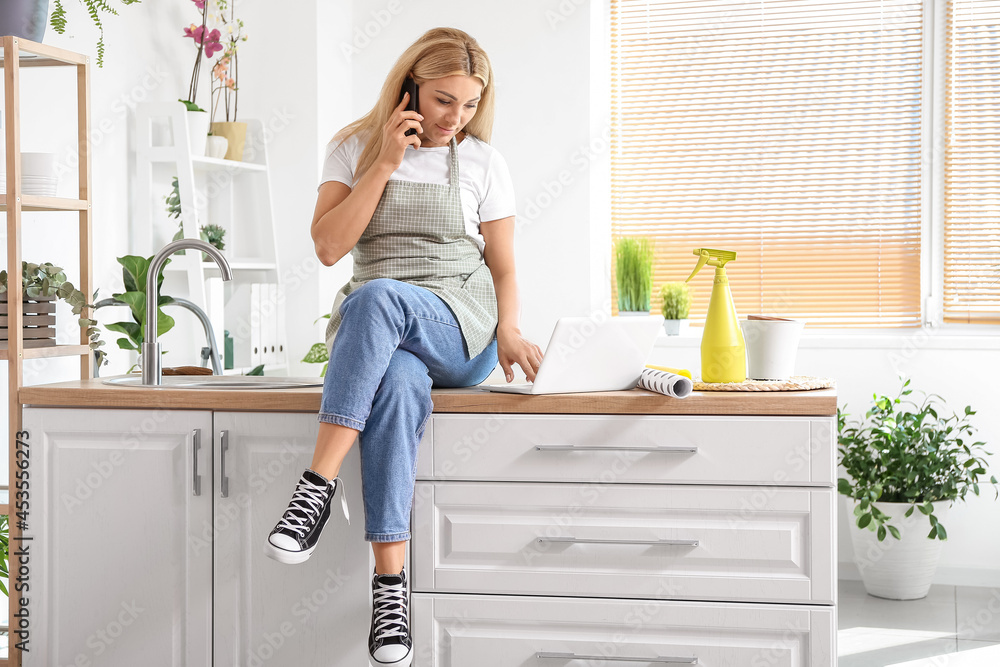 Female gardener with laptop talking by phone at home