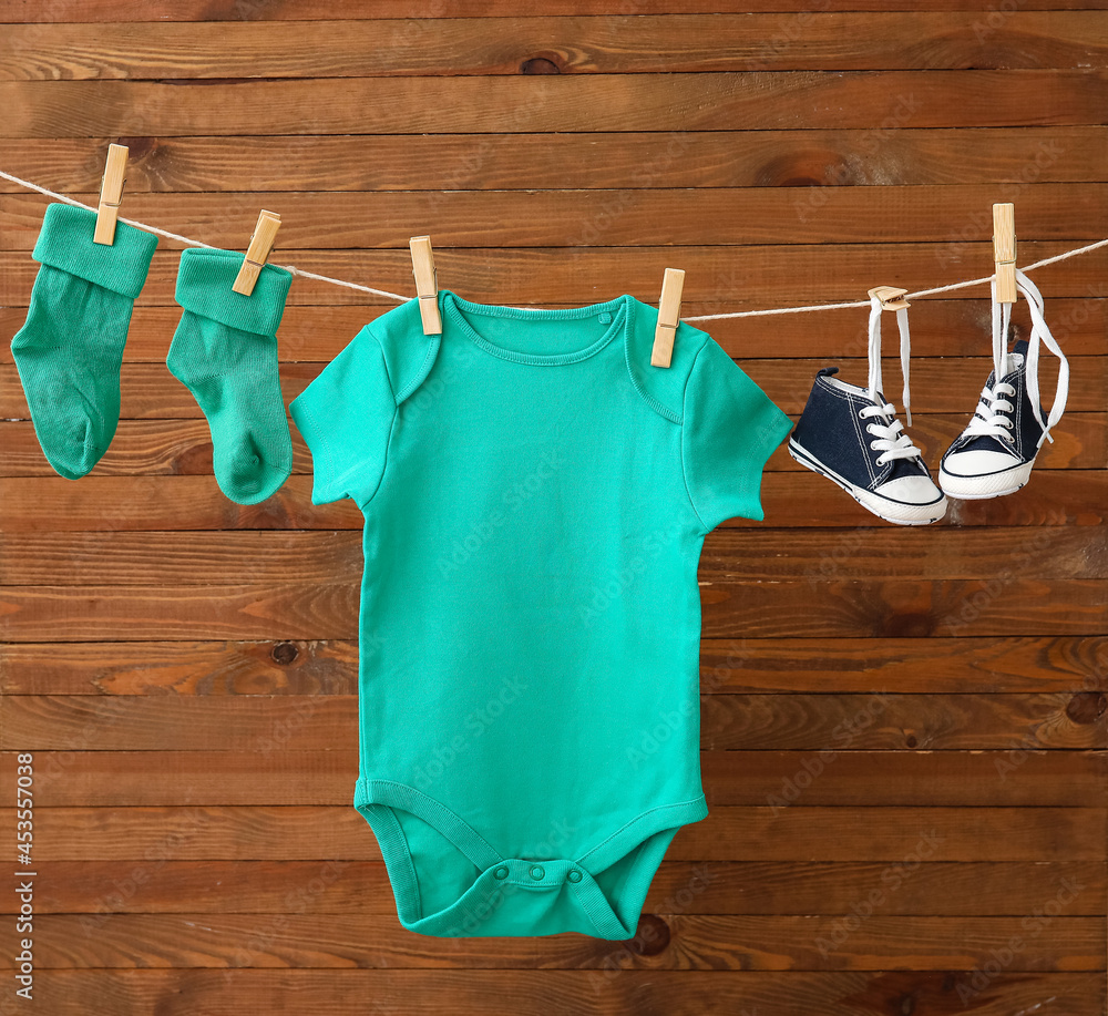 Baby clothes and shoes hanging on rope against wooden background