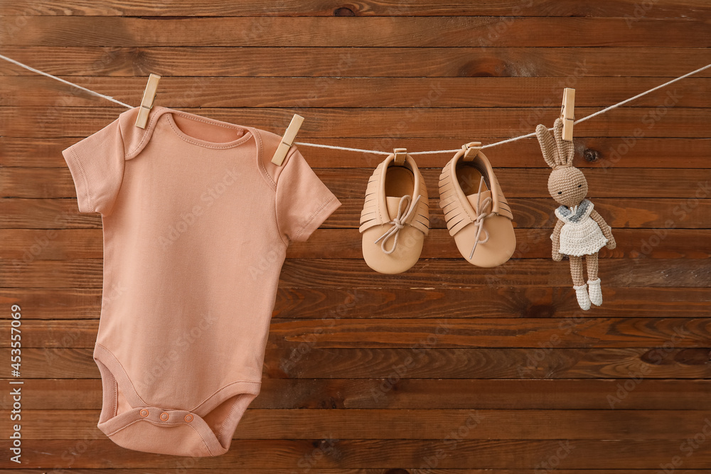 Baby clothes, shoes and toy hanging on rope against wooden background