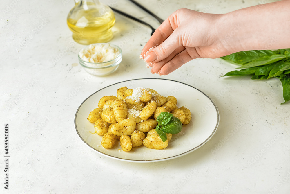 Woman decorating tasty pesto gnocchi with cheese on light background, closeup