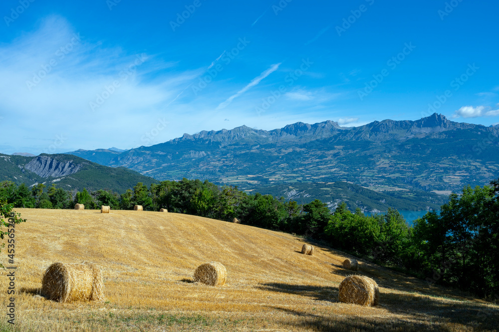 Paysage avec un champ moissoné avec des bales de paille entouré de montagne autour du village de Le 