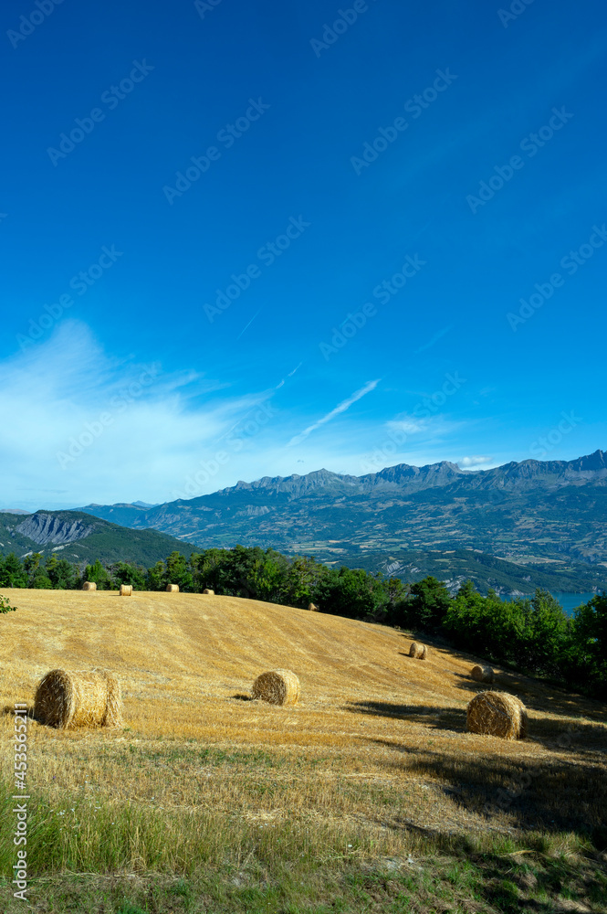 Paysage avec un champ moissoné avec des bales de paille entouré de montagne autour du village de Le 