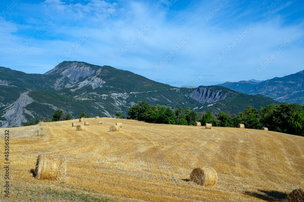 Paysage avec un champ moissoné avec des bales de paille entouré de montagne autour du village de Le 