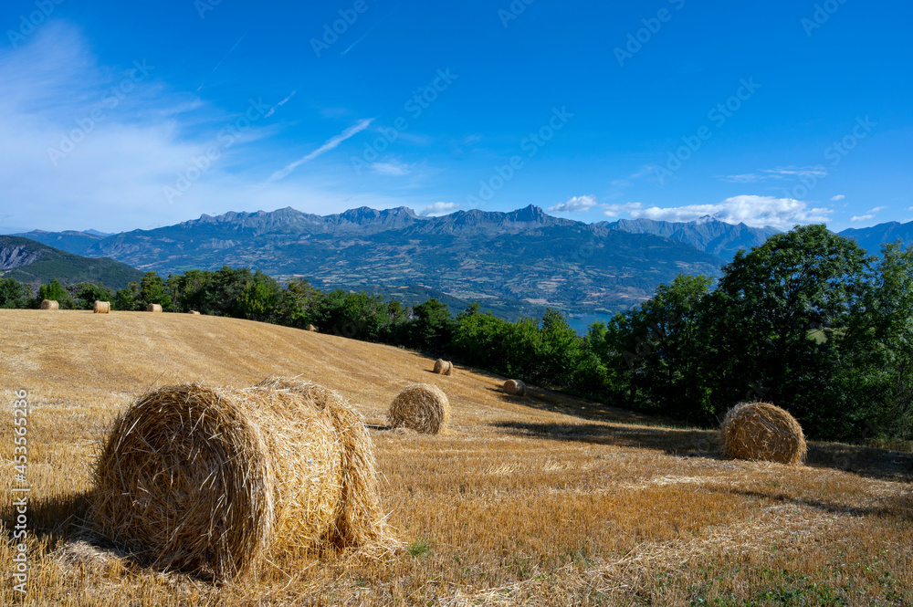 Paysage avec un champ moissoné avec des bales de paille entouré de montagne autour du village de Le 