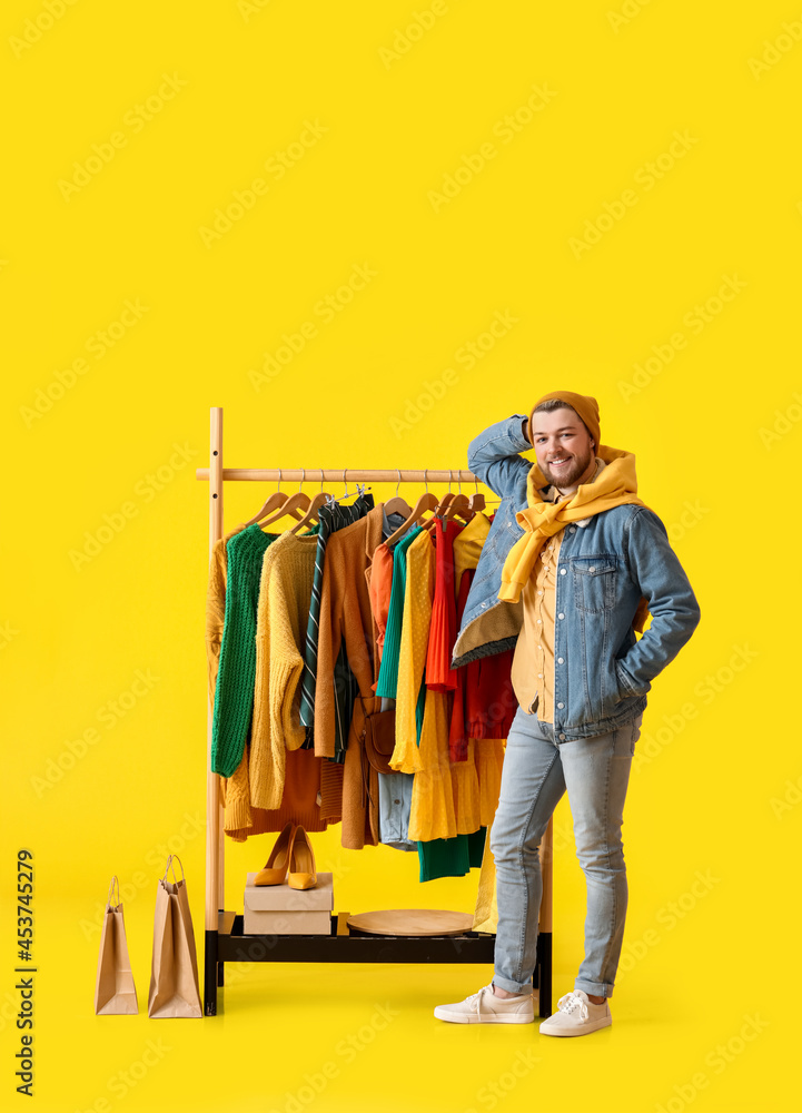 Male stylist near rack with clothes on color background