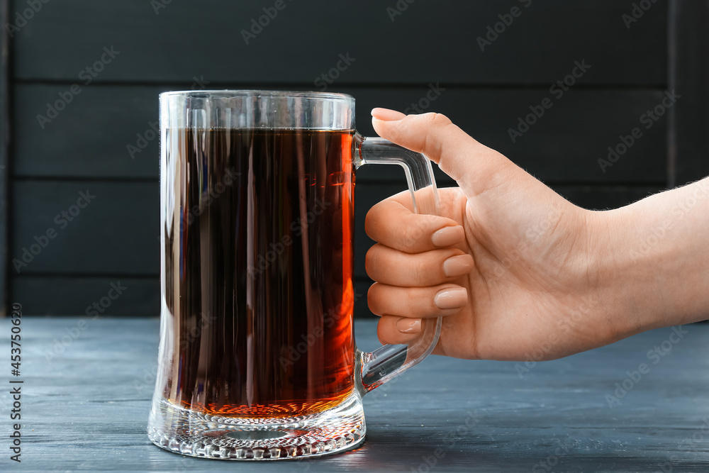 Female hand with mug of fresh kvass on dark wooden background