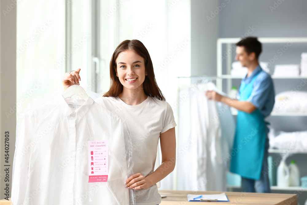 Young woman with clean clothes at modern dry-cleaners