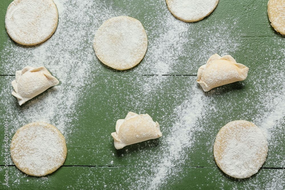 Raw dumplings and fresh dough on color wooden background