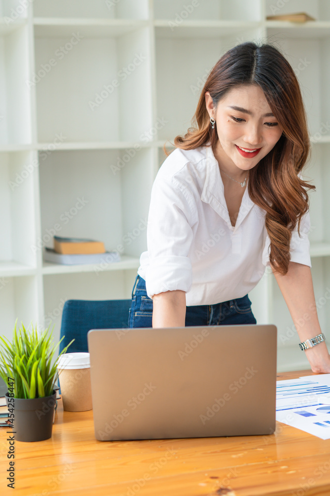 年轻的亚洲商务女性在办公室用笔记本电脑工作，桌上放着文件