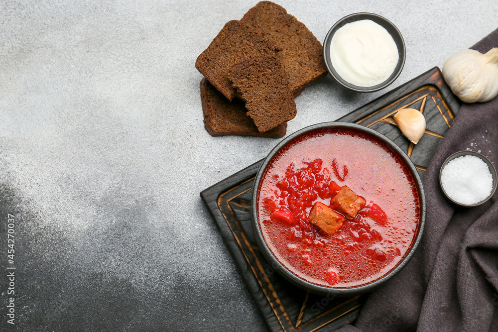 Bowl of tasty borscht, sour cream, bread, salt and garlic on black and white background