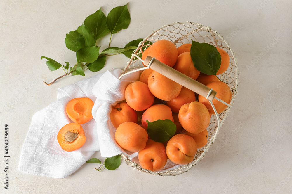 Basket with tasty ripe apricots on light background