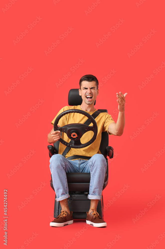 Angry man in car seat and with steering wheel on color background